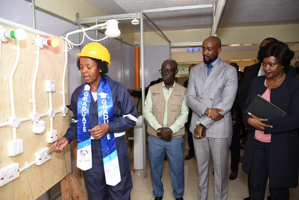 USAID Tumikia Mtoto Project electrical beneficiary Jackline Wanjiku demonstrates to World Vision Kenya National Director Gibert Kamanga, Kasarani MP Ronald Karauri and Family Bank CEO Rebecca Mbithi during the graduation ceremony of 100 young women trained in vocational and technical skills. 